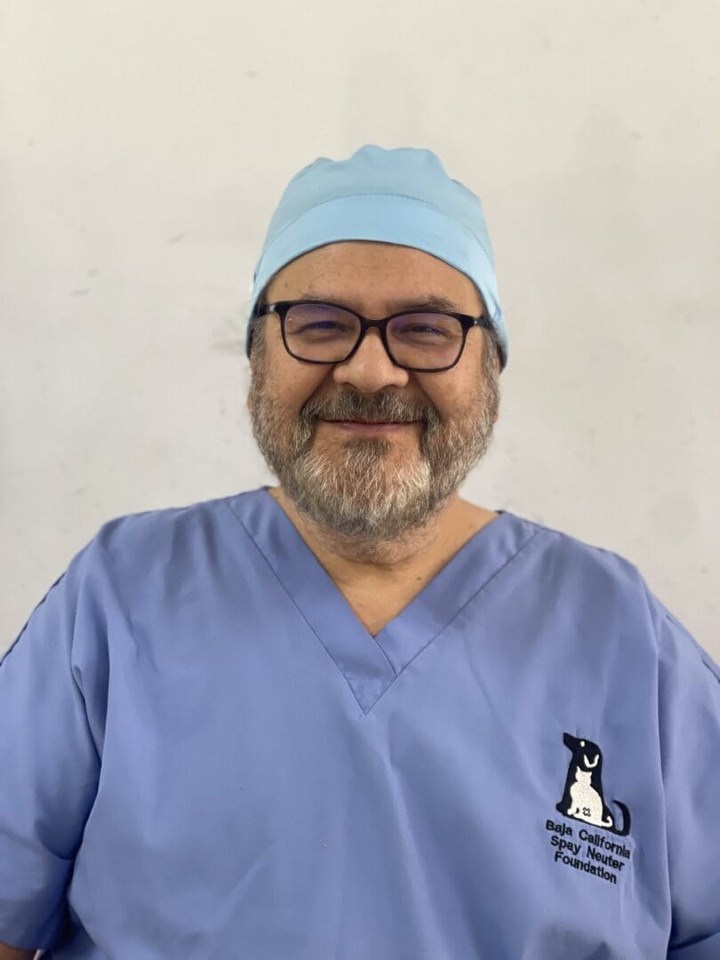 A man in blue scrubs and glasses wearing a hat.