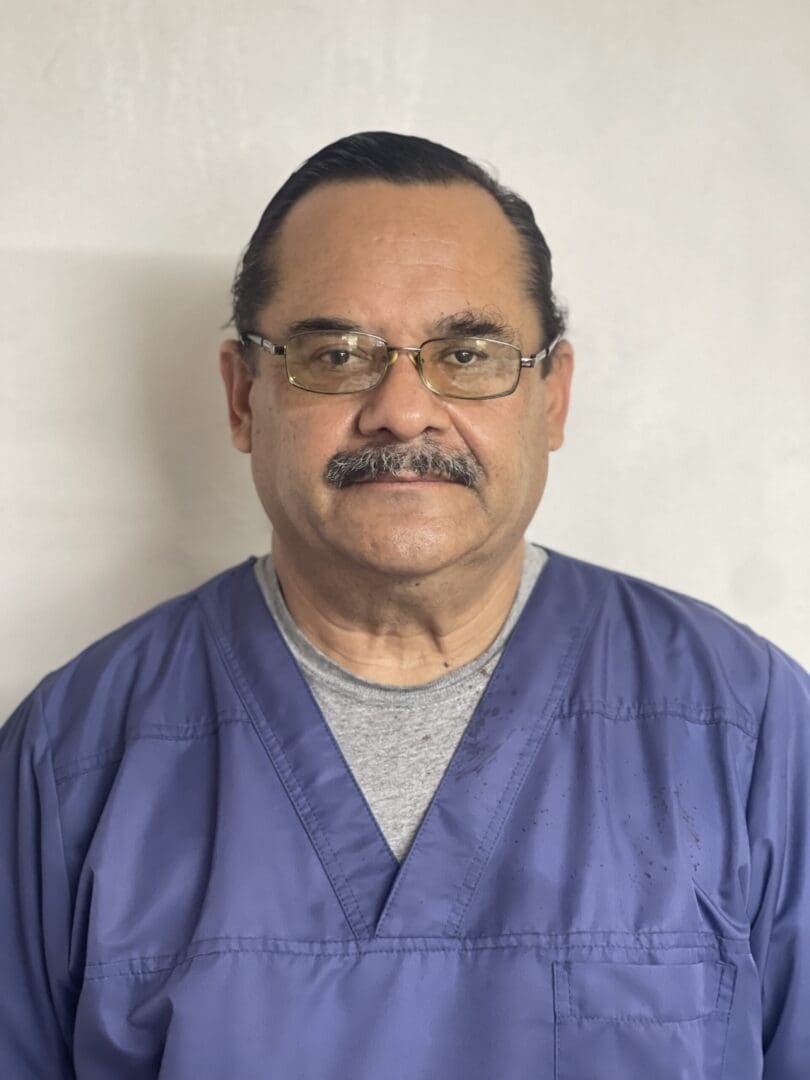 A man in blue scrubs and glasses is posing for the camera.